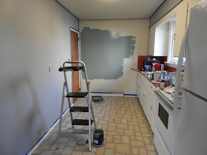 Kitchen remodel in progress with painting supplies and a ladder.